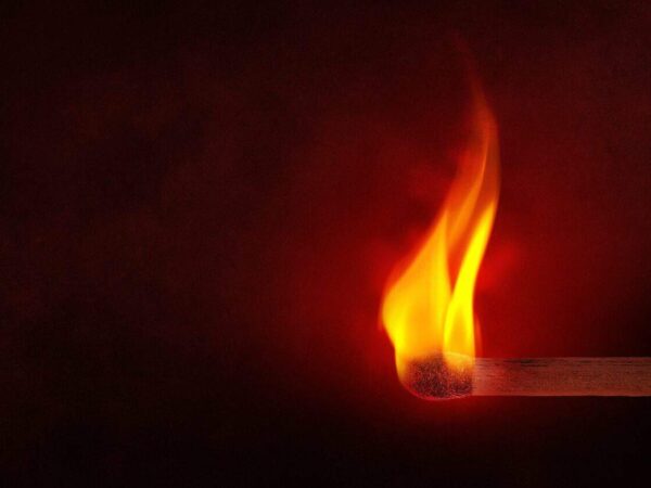 A lit match burning against a dark red background