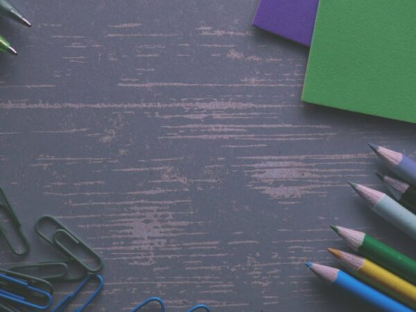 Coloured pencils, paper clips and green paper on a dark wooden desk