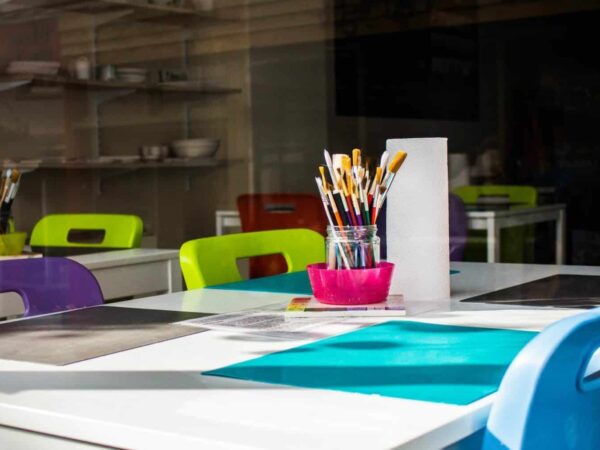 Classroom art supplies on a table | Science Safety Classroom table with art supplies, pencils and markers in cups, and colourful chairs