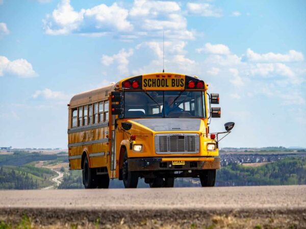 Yellow school bus on a road under a blue sky with clouds