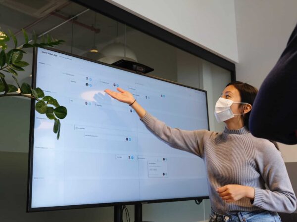 Presenter wearing a face mask pointing at a large display screen