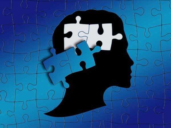 Silhouette of a head with a missing puzzle piece, on a blue puzzle background