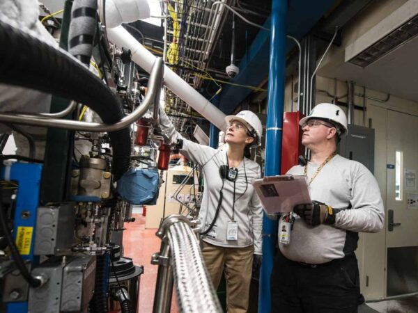 Two workers in hard hats checking equipment in an industrial plant