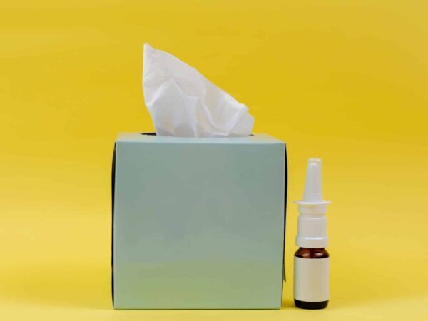 Box of tissues and a nasal spray bottle on a yellow background