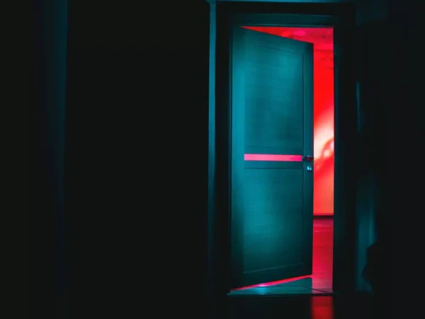 Dark room with a door standing ajar, lit in teal and red