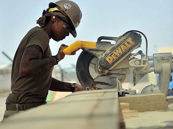 Soldier in a hard hat and safety glasses cutting lumber with a mitre saw