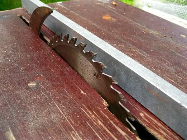 Table saw blade rising through a worn wooden table