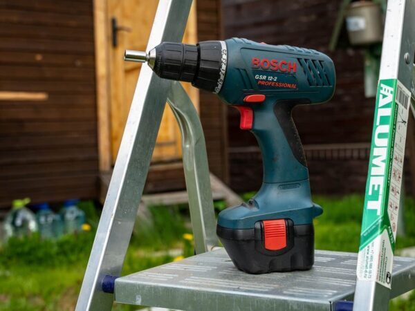 Cordless drill resting on the step of an aluminium ladder