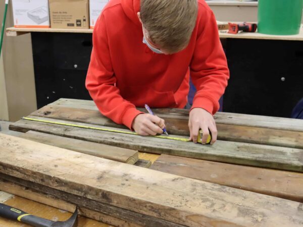 Woodshop student measuring a board | Science Safety Student marking a board in a woodshop