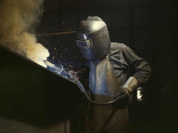 Welder in a protective mask working amid sparks and smoke in a dark factory