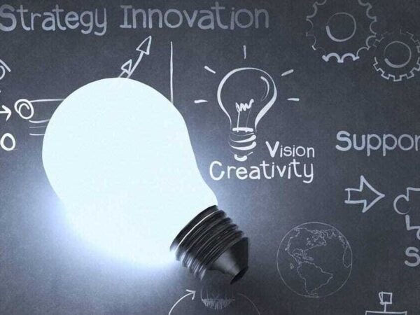 Glowing light bulb on a chalkboard with the words strategy, innovation, vision, creativity and support