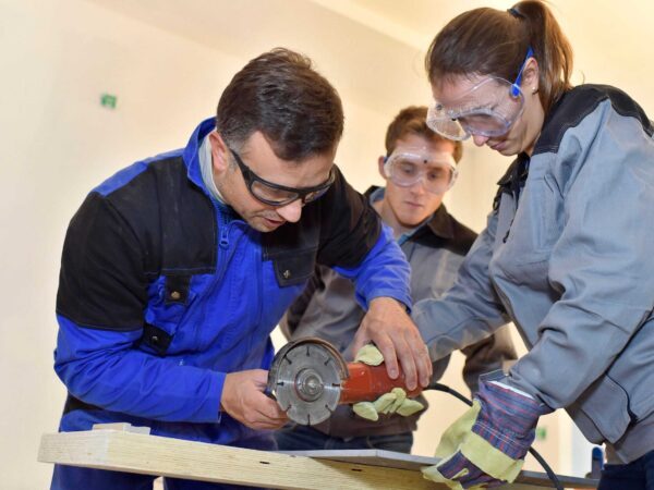 CTE Department Chair Pathway | Science Safety Instructor in safety glasses guiding a student using a power tool in a workshop