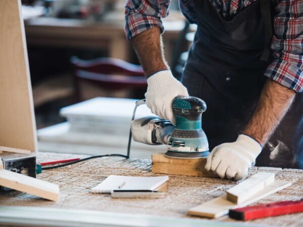 Gloved hands using an orbital sander on a piece of wood