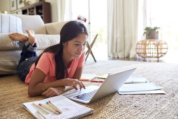 Student working on a laptop on the floor at home