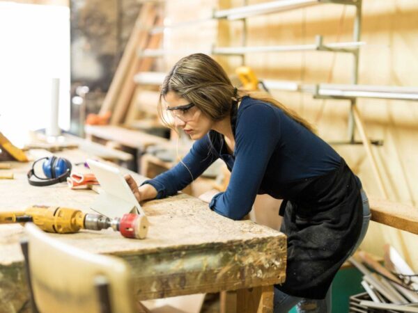 Carpenter using a tablet for work | Science Safety Woman in safety glasses working at a carpentry bench in a workshop