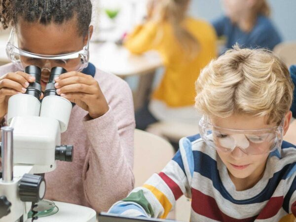 Elementary students with a microscope and a tablet | Science Safety Elementary students in safety glasses, one looking into a microscope and one using a tablet