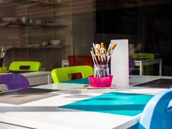 Classroom table with art supplies, pencils and markers in cups, and colourful chairs