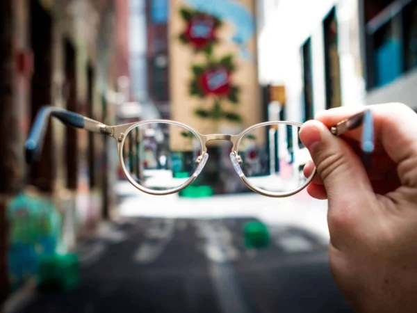 Hand holding a pair of glasses up to a blurred street scene