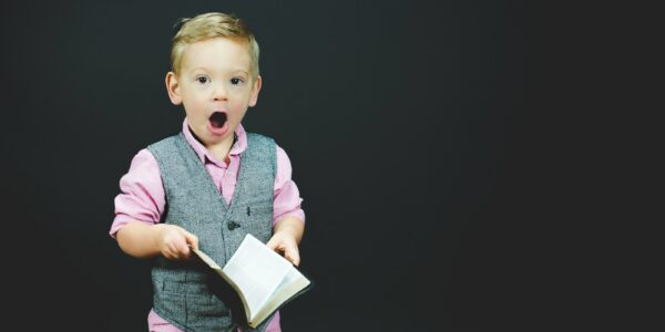 boy wearing gray vest and pink dress shirt holding book