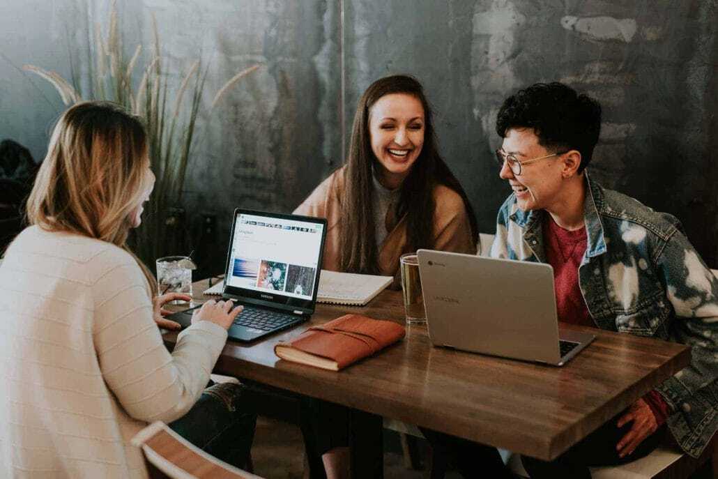 Three people talking and working on laptops at a table
