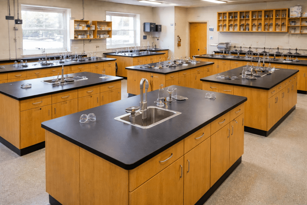 A science laboratory classroom with wooden workstations, sinks, stools, shelves with equipment, and large windows providing natural light—carefully designed to prevent overcrowding and ensure a safe occupancy load.