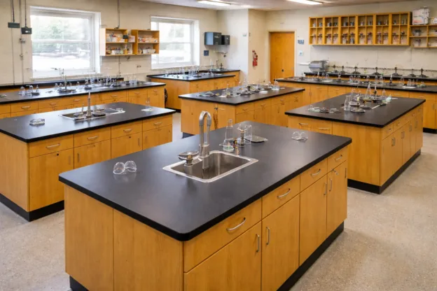 A science laboratory classroom with wooden workstations, sinks, stools, shelves with equipment, and large windows providing natural light—carefully designed to prevent overcrowding and ensure a safe occupancy load.