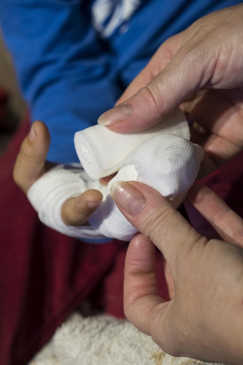 Adult hands wrapping a white bandage around a child's injured hand