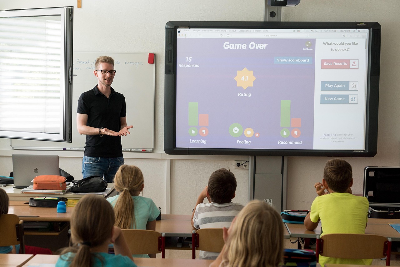 Teacher presenting to an elementary class beside a large screen